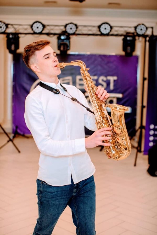 Портрет музиканта Стаса в білій сорочці, який грає на своєму золотому саксофоні