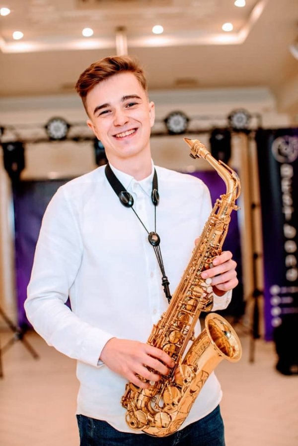 Радісний та усміхнений саксофоніст Стас музичного гурту Бест Бенд зі своїм саксофоном